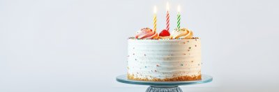 Birthday cake with colorful candles and decorations on a glass stand set against a minimalist backdrop